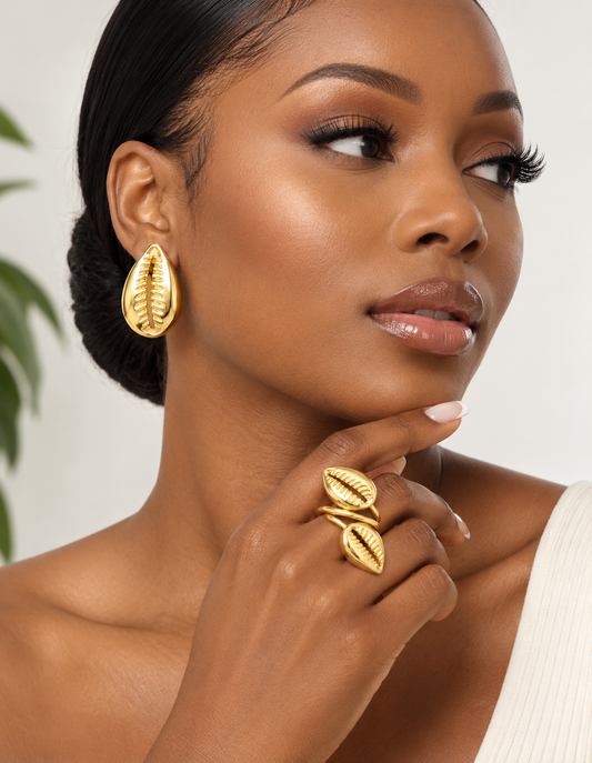 Woman wearing gold cowrie-shaped earrings and a matching adjustable two-shell ring