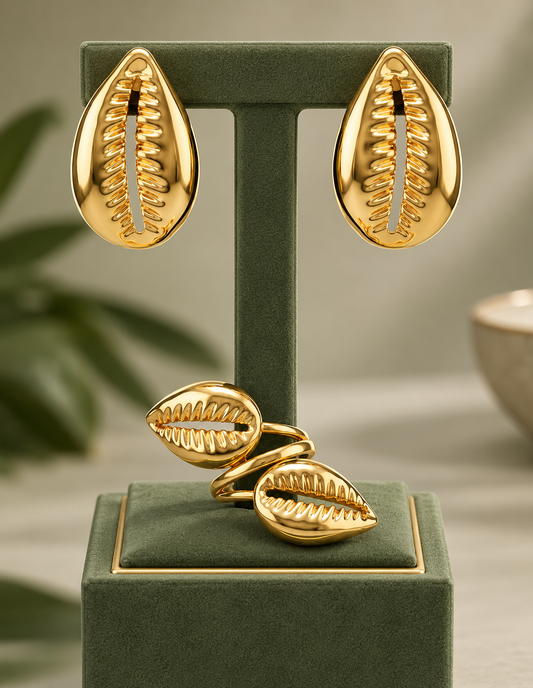 Gold cowrie-shaped earrings and adjustable ring on a green jewelry display
