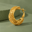 Angled view of a patterned gold hoop earring on sage-green fabric