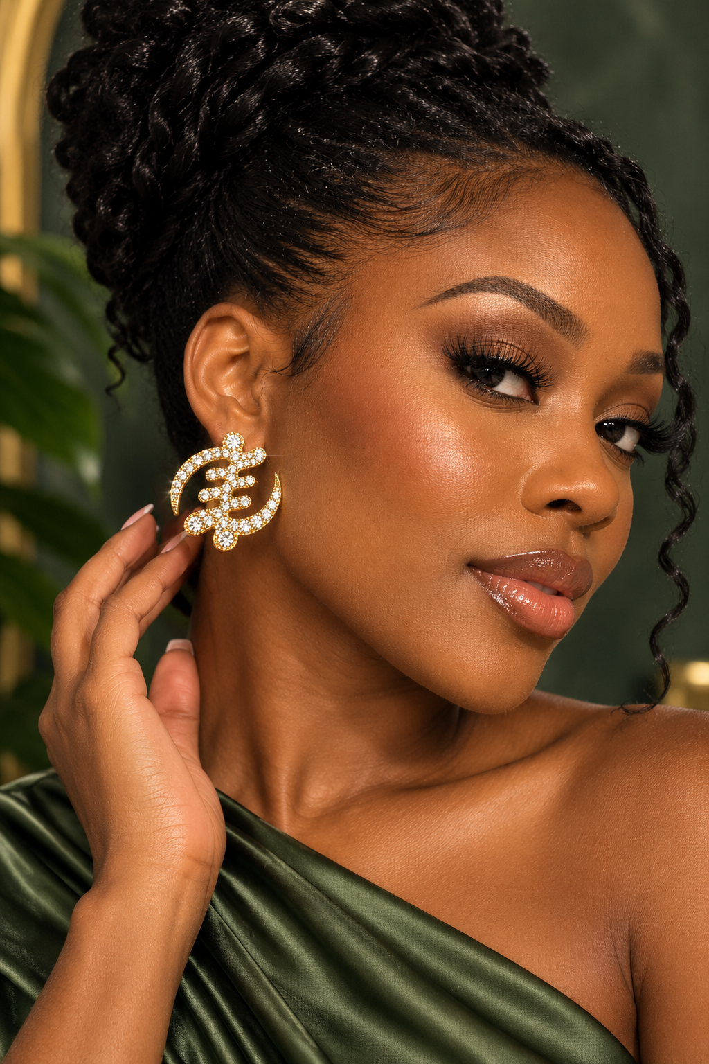 Woman wearing crystal-studded gold Gye Nyame earrings with a green one-shoulder top