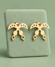 Pair of gold Akofena crossed-sword stud earrings on a pale green display
