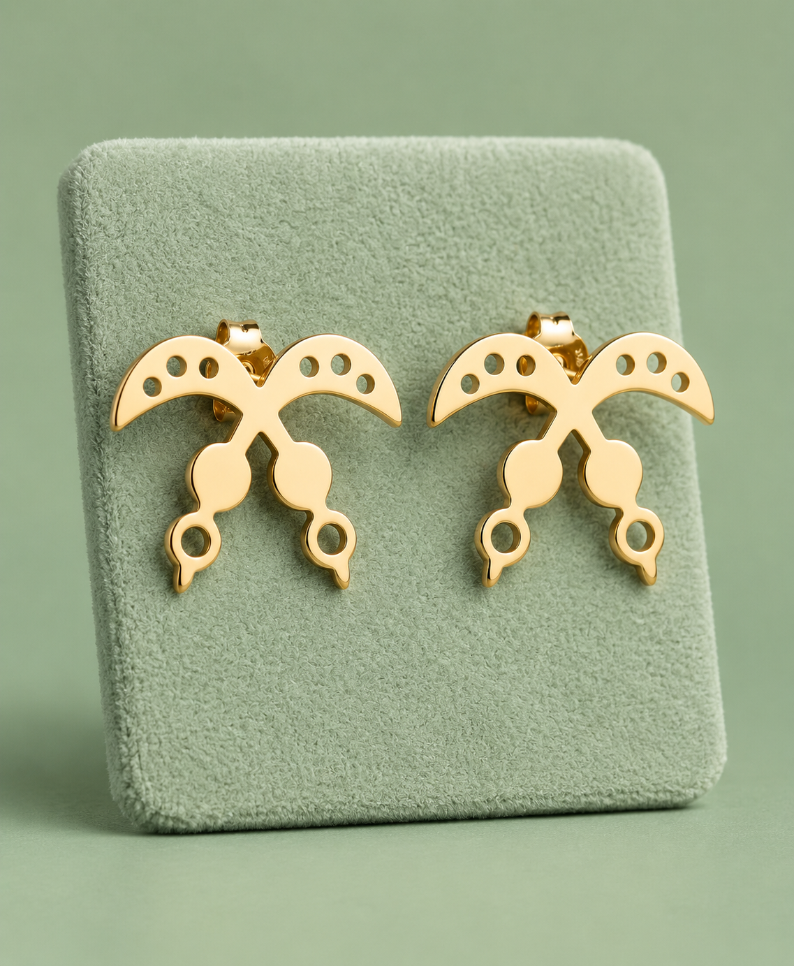 Pair of gold Akofena crossed-sword stud earrings on a pale green display
