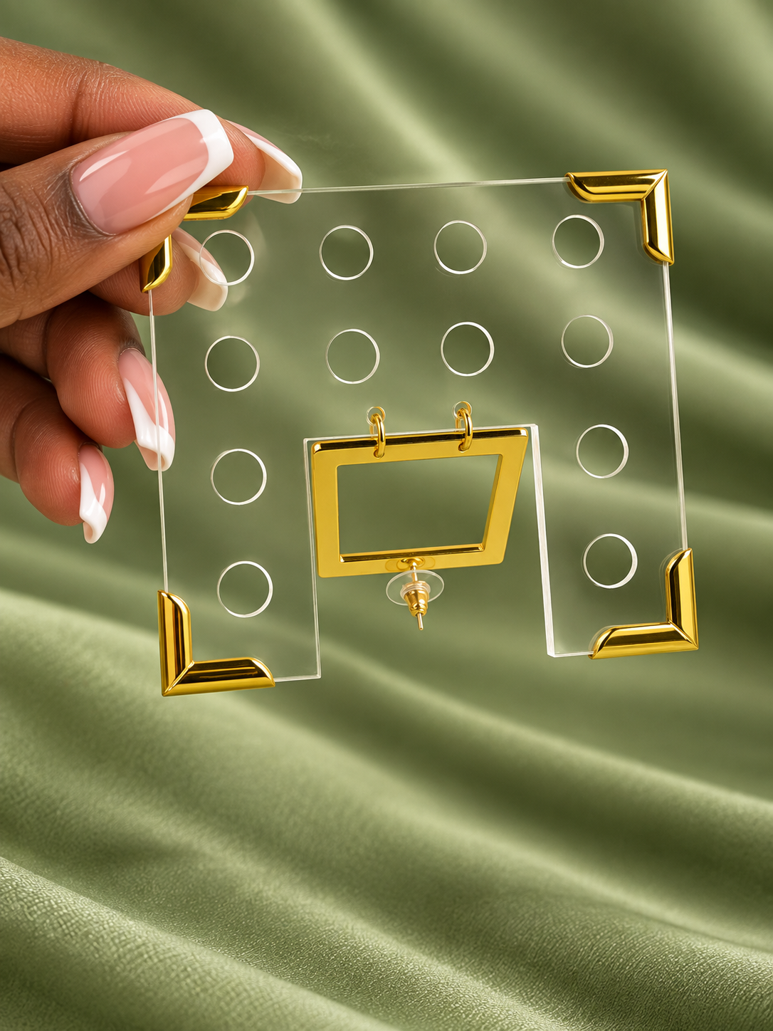 Hand holding a clear square Geo earring with circular cutouts and gold-tone corners
