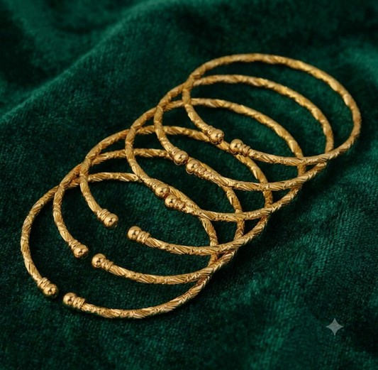 Six textured gold-plated bangles arranged on green velvet