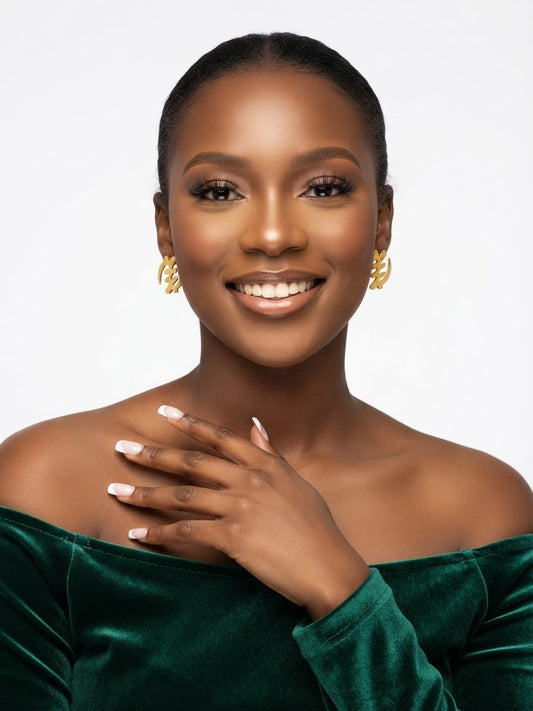 Woman wearing small gold Gye Nyame stud earrings with a dark green velvet top