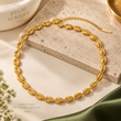 Gold cowrie-link choker necklace with an extension chain arranged on cream-colored stone