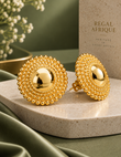 Gold Nubian Goddess jumbo stud earrings on a round stone display beside Regal Afrique packaging