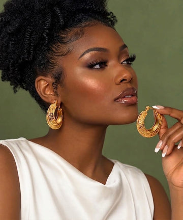 Woman wearing a patterned gold hoop earring and holding the matching hoop
